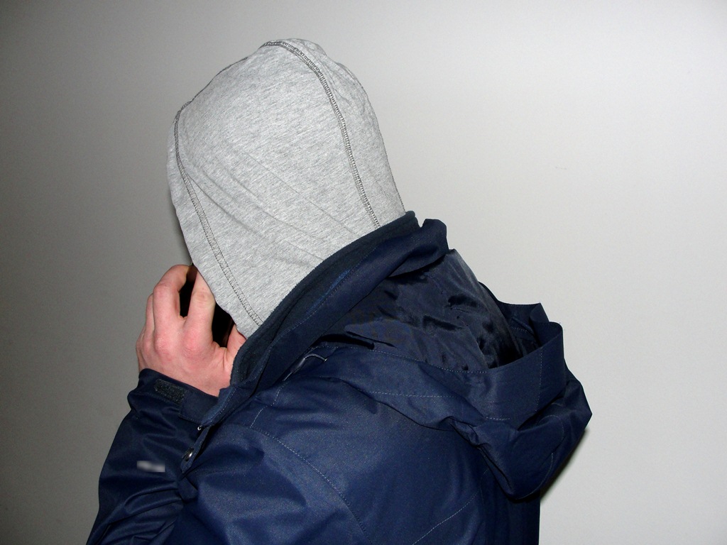 Mężczyzna w bluzie w kapturem na głowie rozmawia przez telefon komórkowy - fot. KMP Nowy Sącz
